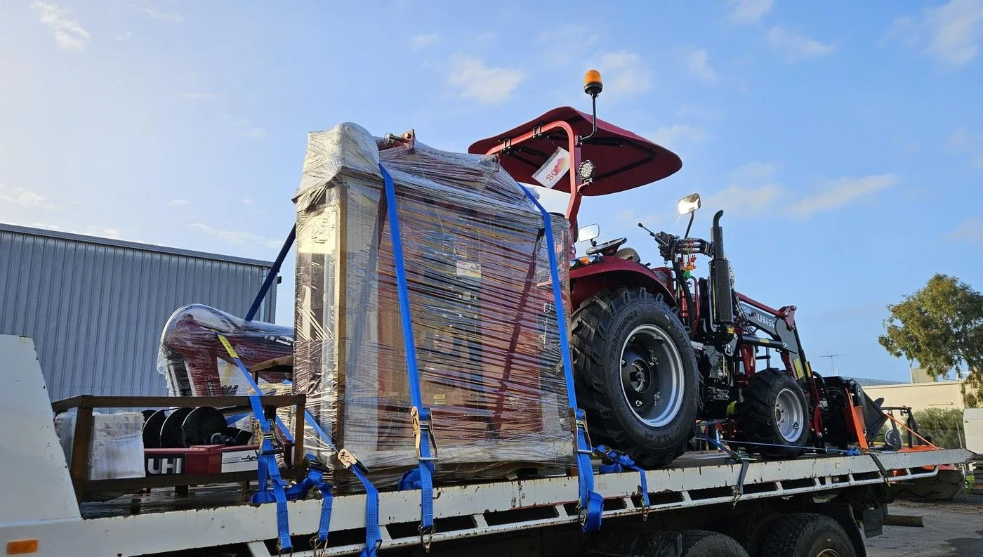 Red tractor and wrapped farm equipment secured on a flatbed truck.