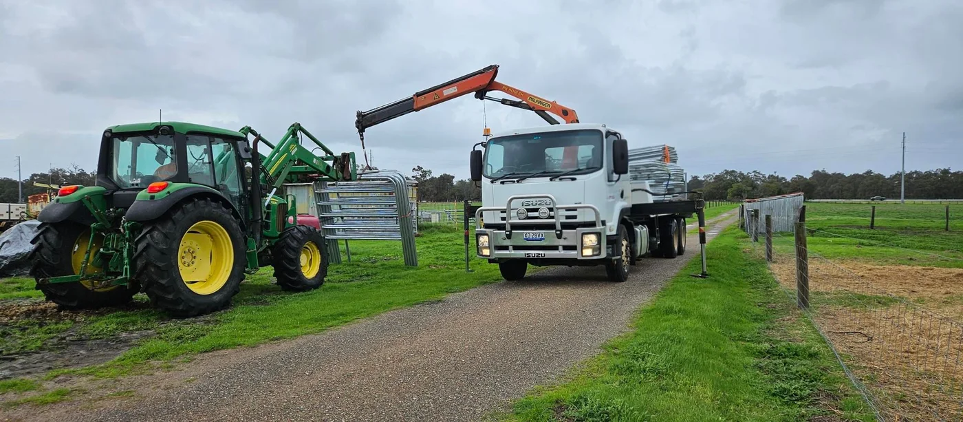 Hiab crane lifting cattle fencing panels with a tractor assisting on site.