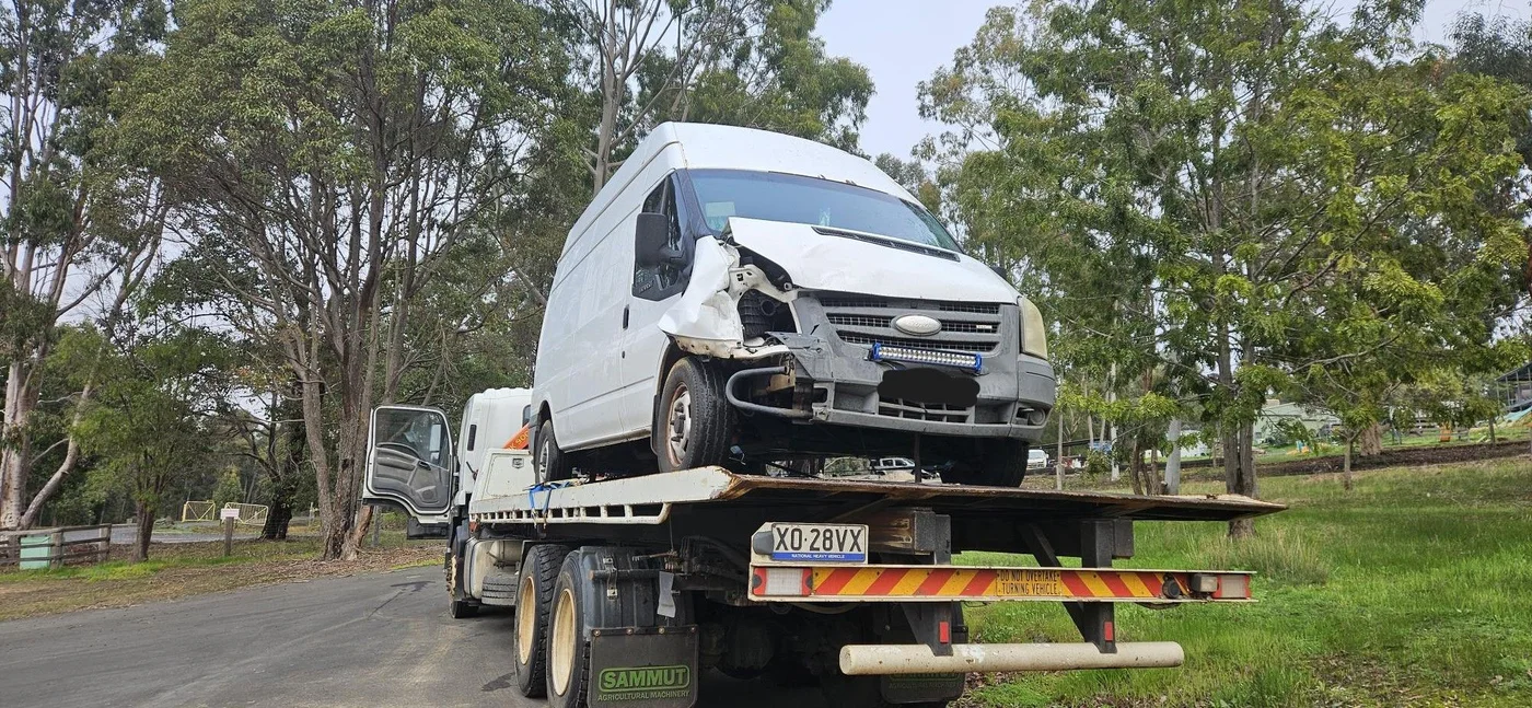 Damaged van loaded on a tilt tray truck in a bush setting.