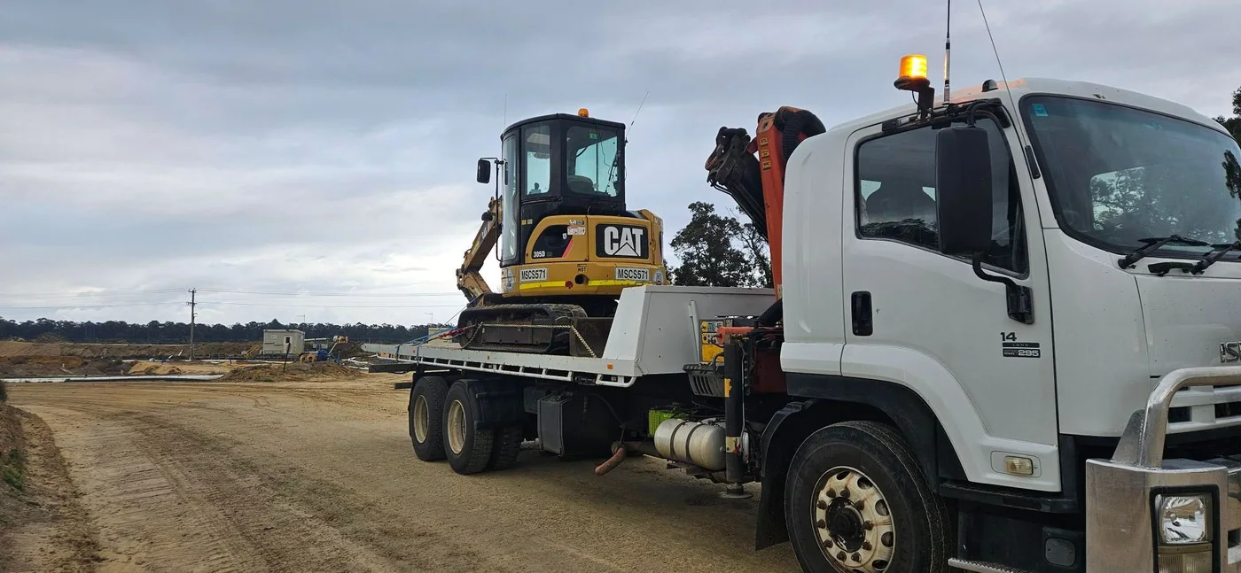 CAT mini excavator secured on a hiab truck at a construction site.