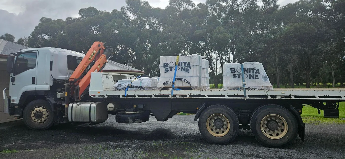Hiab truck carrying palletised stone products secured with straps.