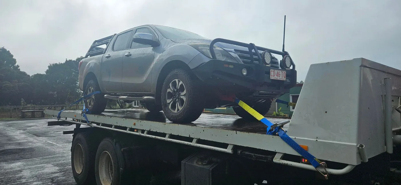 Dual-cab utility vehicle secured on a tilt tray in wet conditions.
