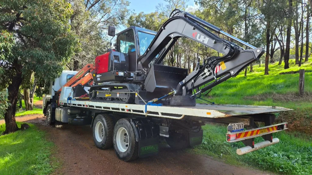 Lane Transport flatbed with a black and red UHI excavator secured on a rural South West track.