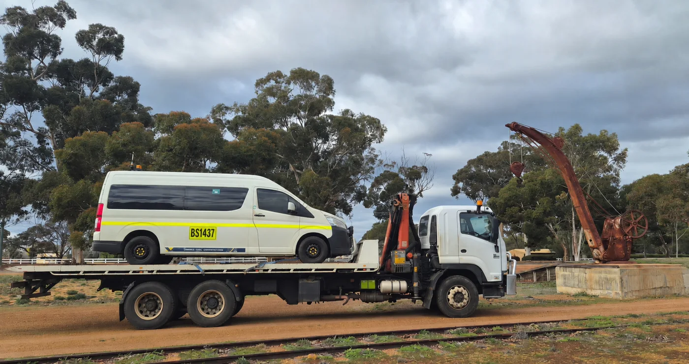 Passenger van secured on a hiab flatbed for vehicle transport.